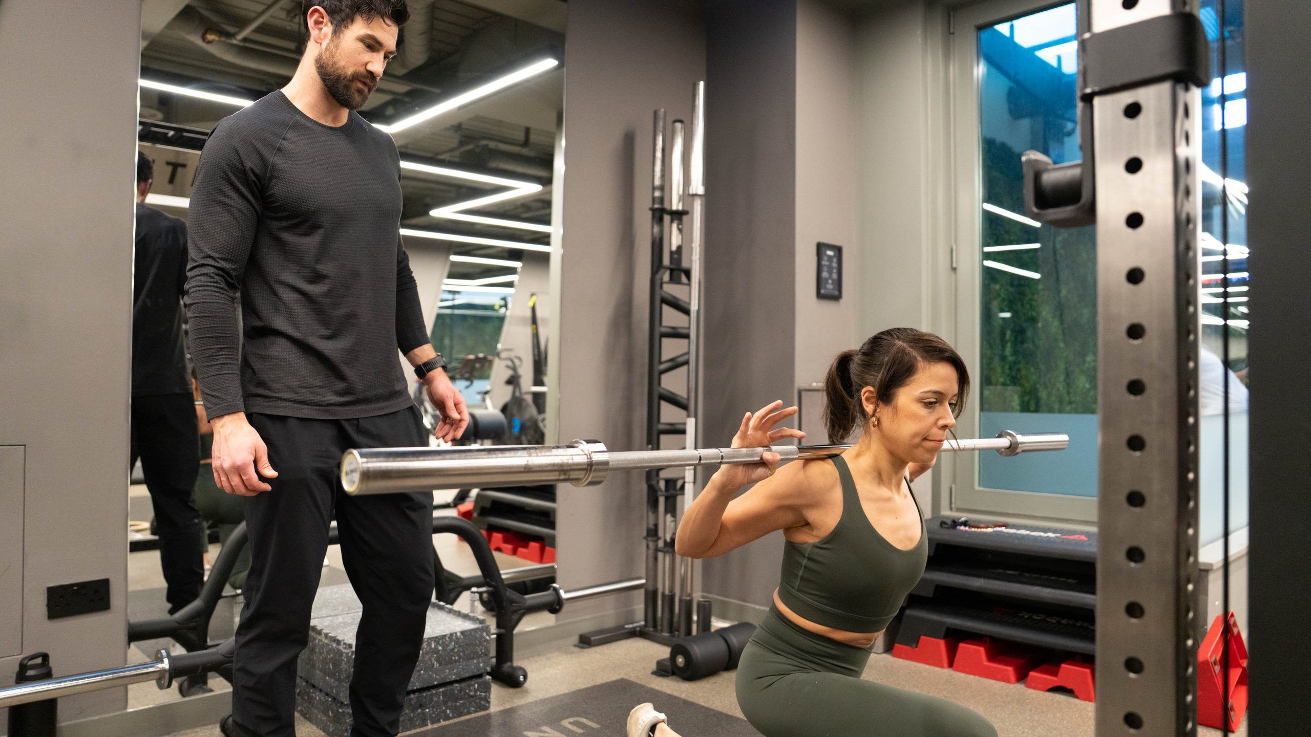 A trainer watching a woman in a low barbell split squat at UNTIL Liverpool Street