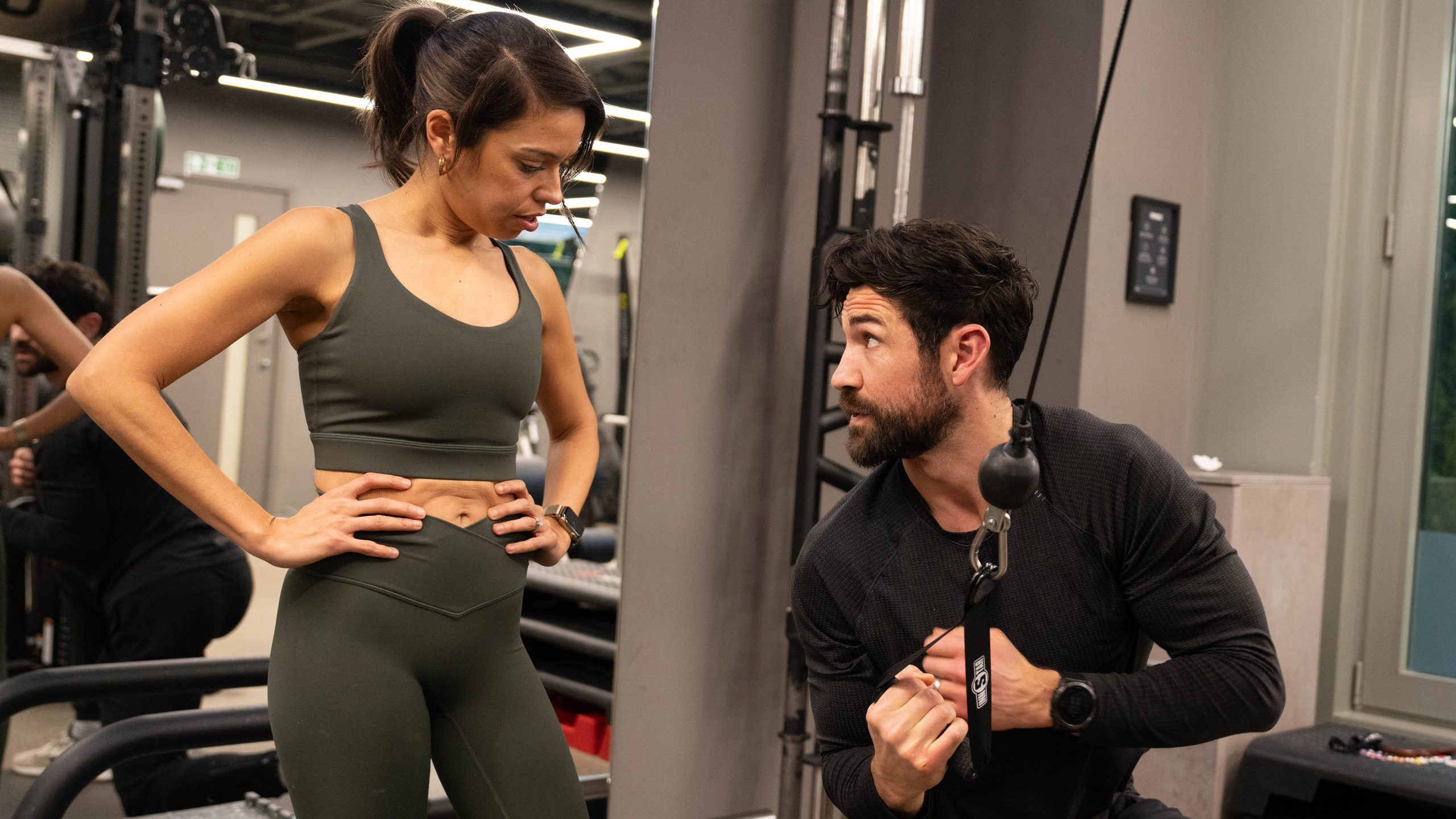 A trainer demonstrating a kneeling cable pull as a client watches