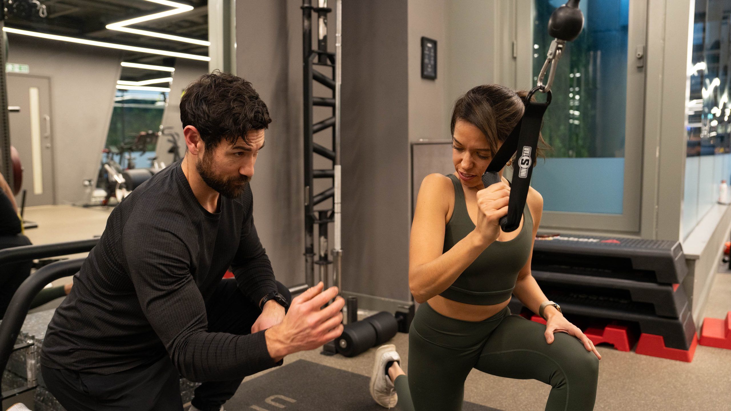 A trainer coaching arm position during a half-kneeling cable pull