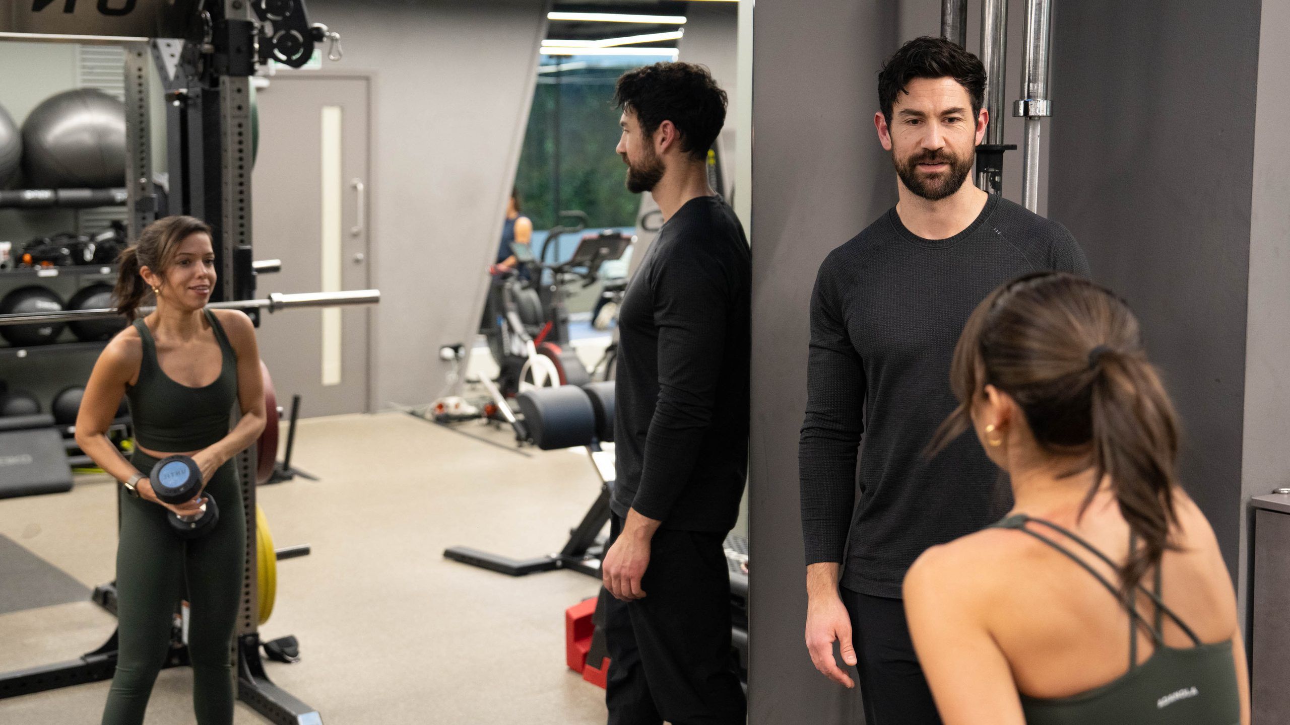 Two trainers watching a woman hold a dumbbell between sets