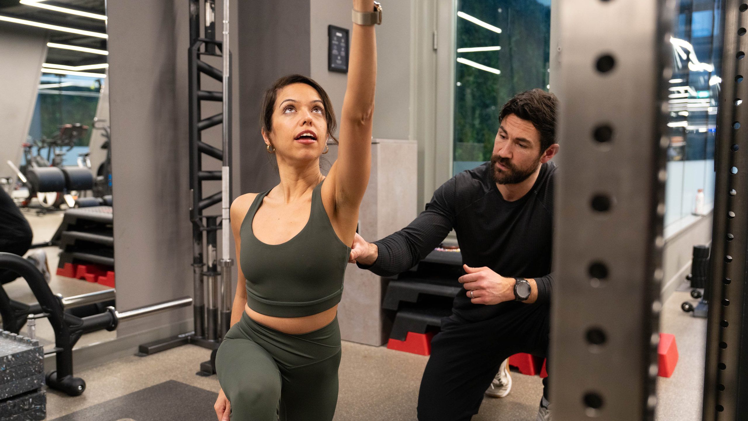 A coach guiding a client's shoulder during an overhead cable reach