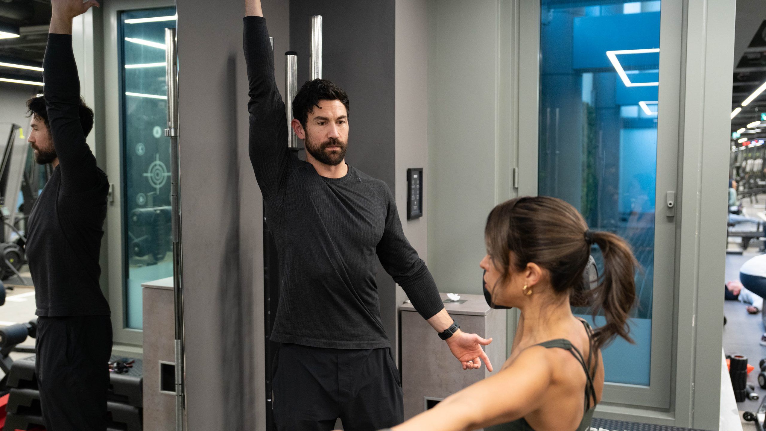 Two coaches demonstrating an overhead reach drill to a client on the training floor