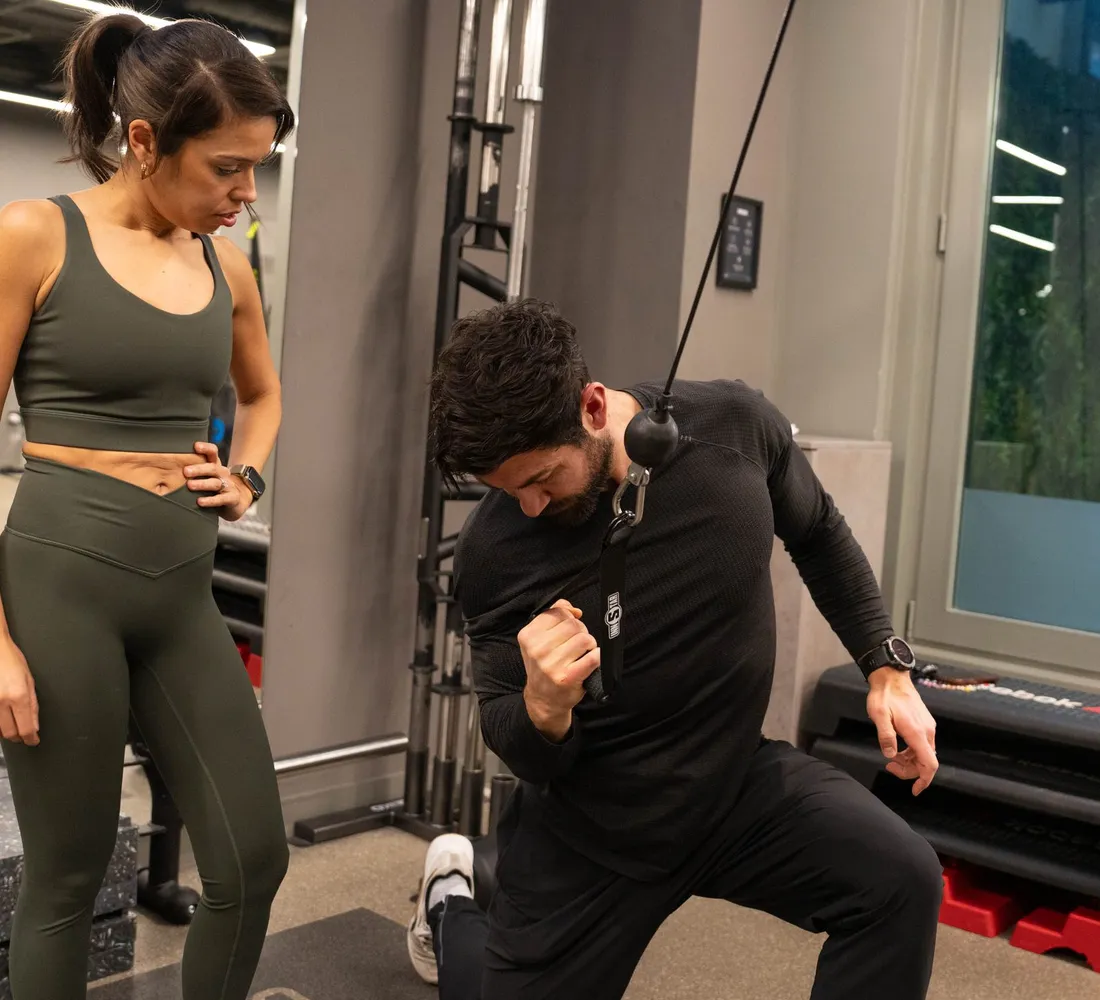 Client watching as a trainer demonstrates a kneeling cable exercise