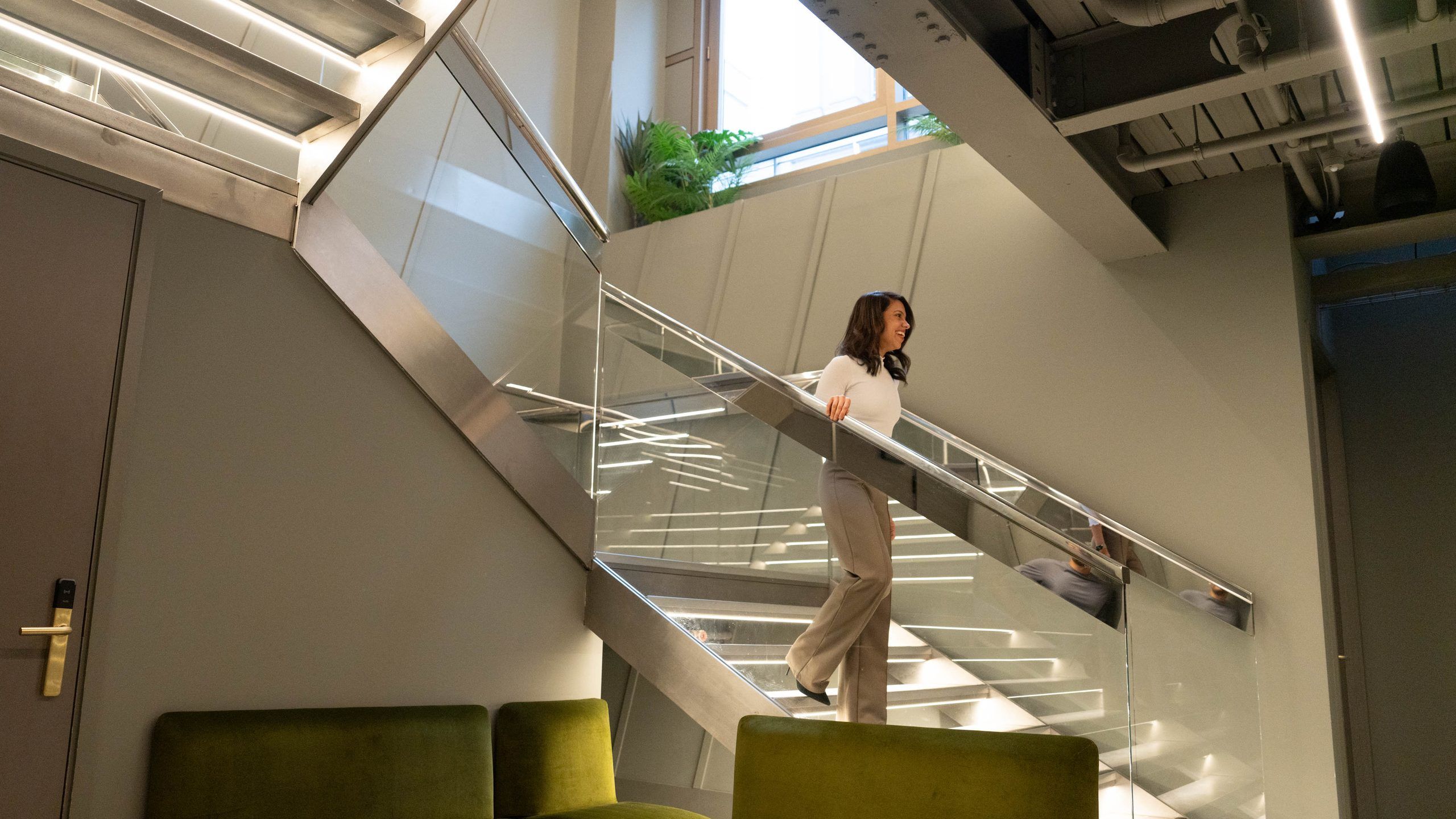 Glass staircase above green lounge seating inside an UNTIL club