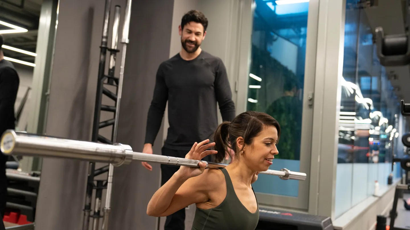 Trainer watching a woman's form as she lowers into a barbell split squat