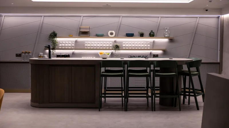 The kitchen counter and bar stools in the club space at UNTIL Liverpool Street, lit from a shelf of glassware behind