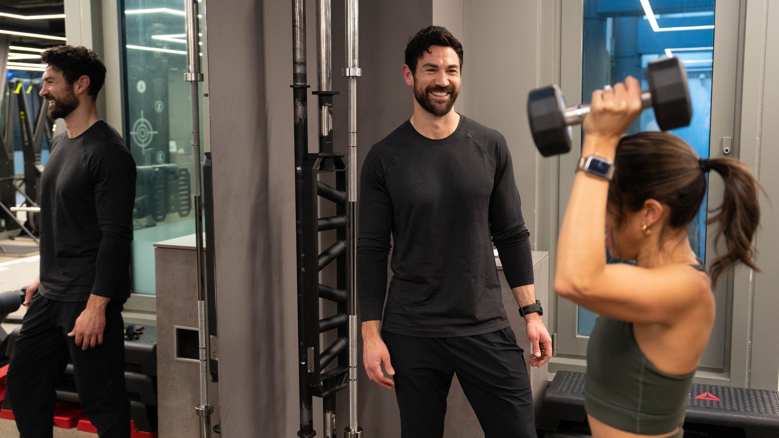 Woman pressing a dumbbell overhead as two trainers look on