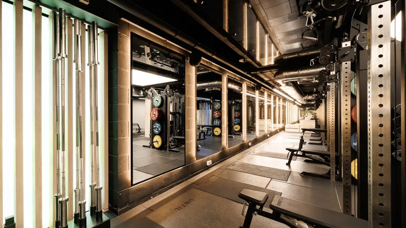 A mirrored training corridor at UNTIL Soho, with rigs and loaded plate racks running down one side under green and warm strip lighting