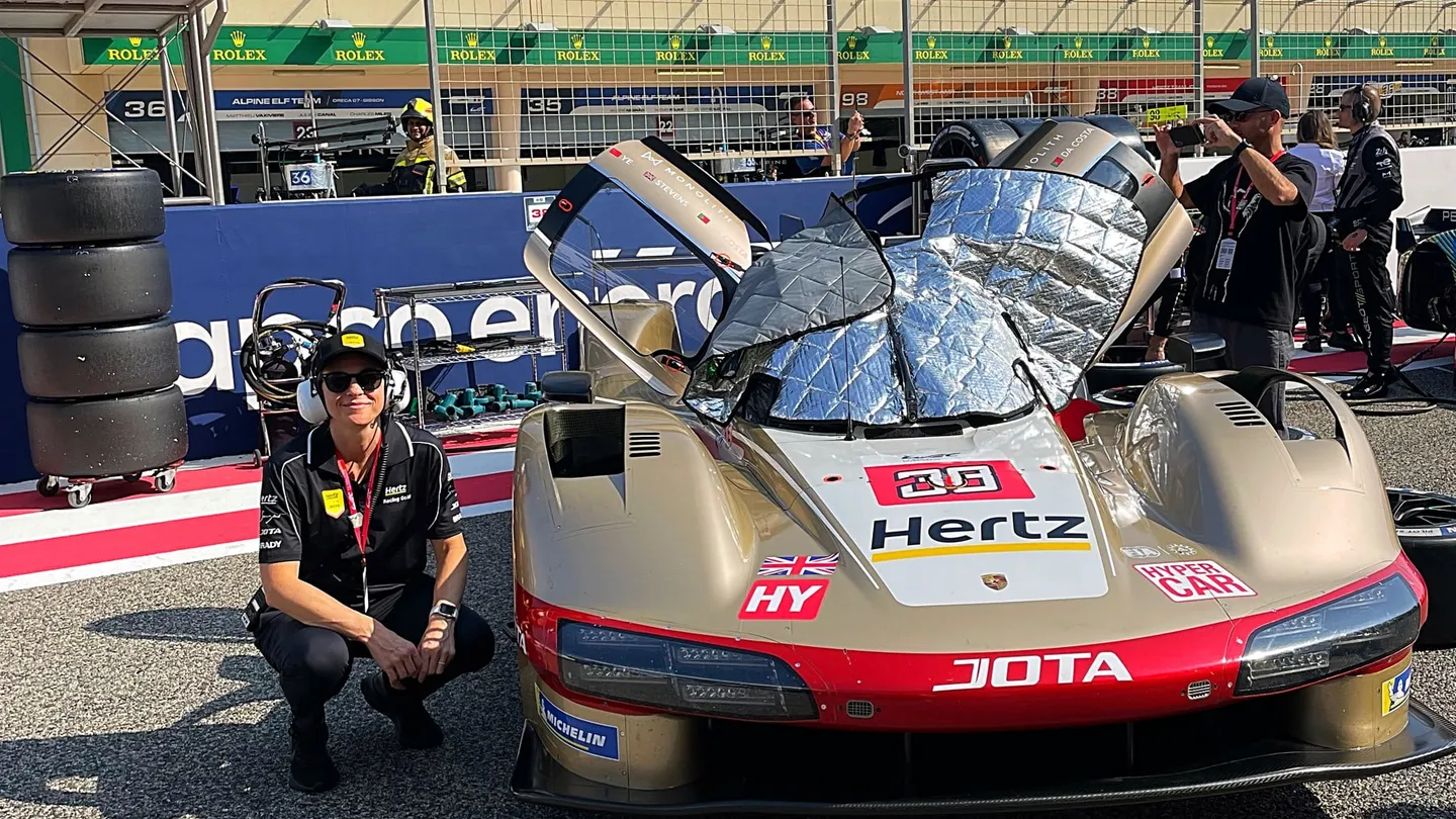 Carly Christensen crouched beside the Hertz Team Jota car on the grid at the 8 Hours of Bahrain 2024