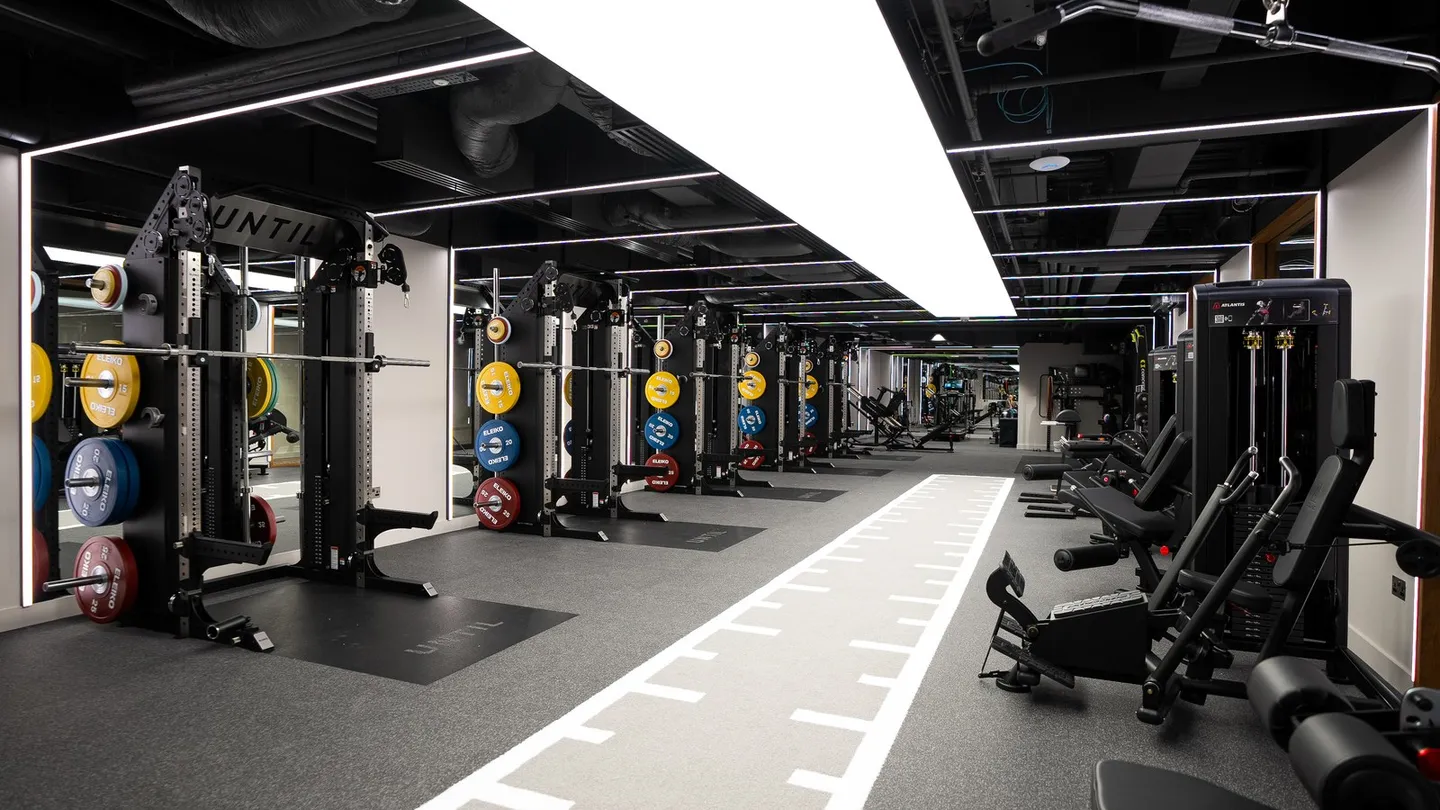 The gym floor at UNTIL Canary Wharf, 30 South Colonnade, London E14: strength racks with coloured weight plates beside a marked sprint track.
