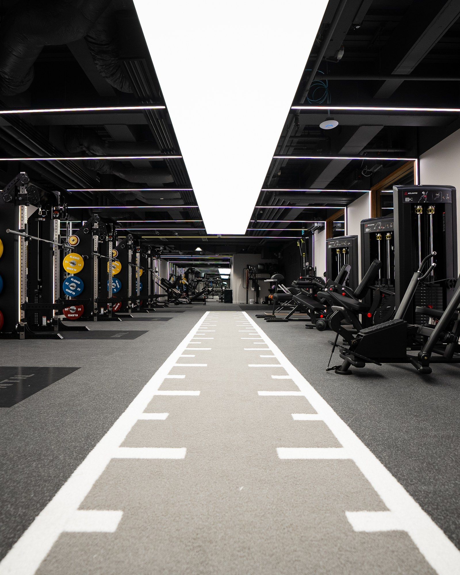 The gym floor at UNTIL Canary Wharf, with a sprint track running between strength racks and resistance machines.