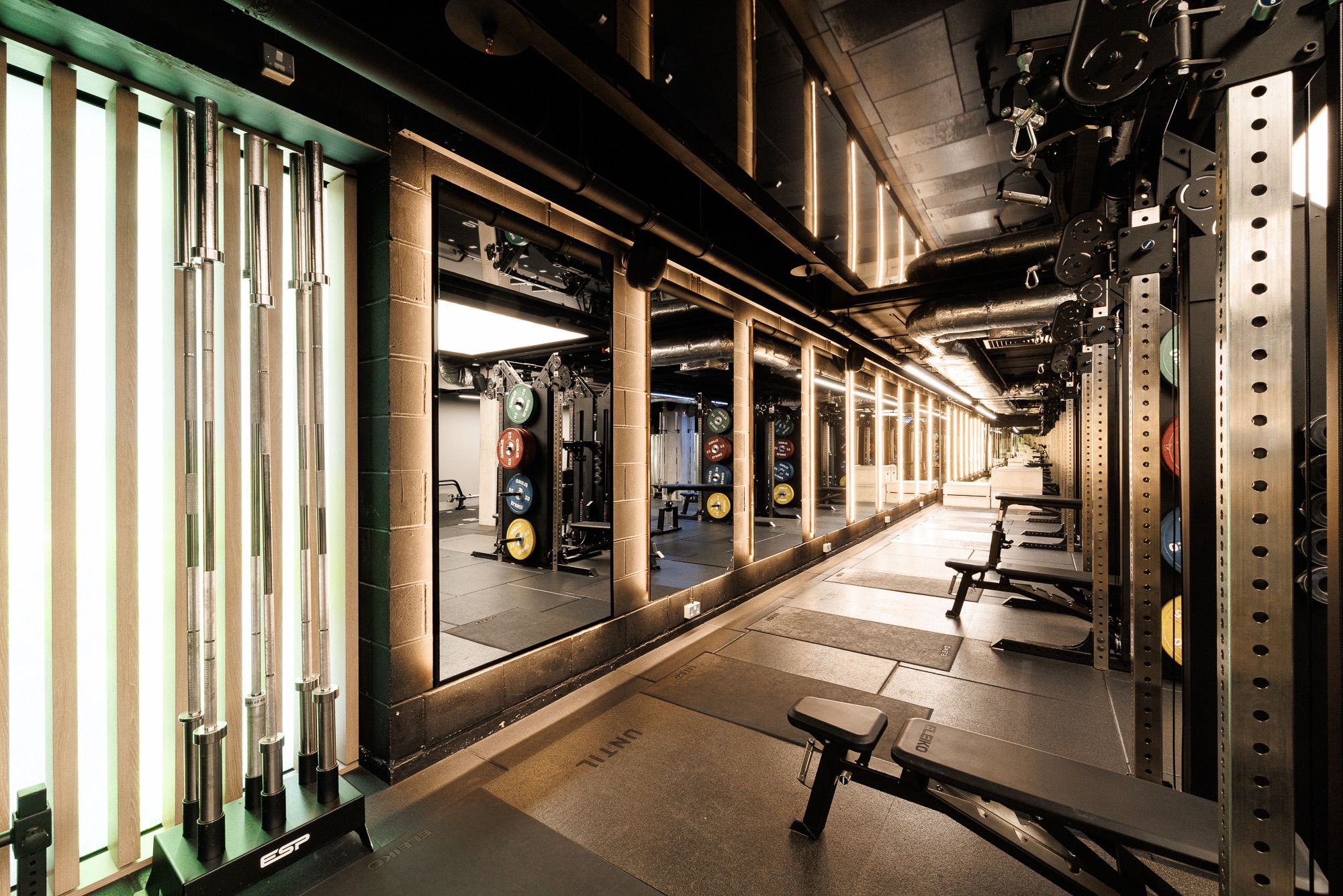 The mirrored barbell floor at UNTIL Soho, with racks, benches and loaded plates