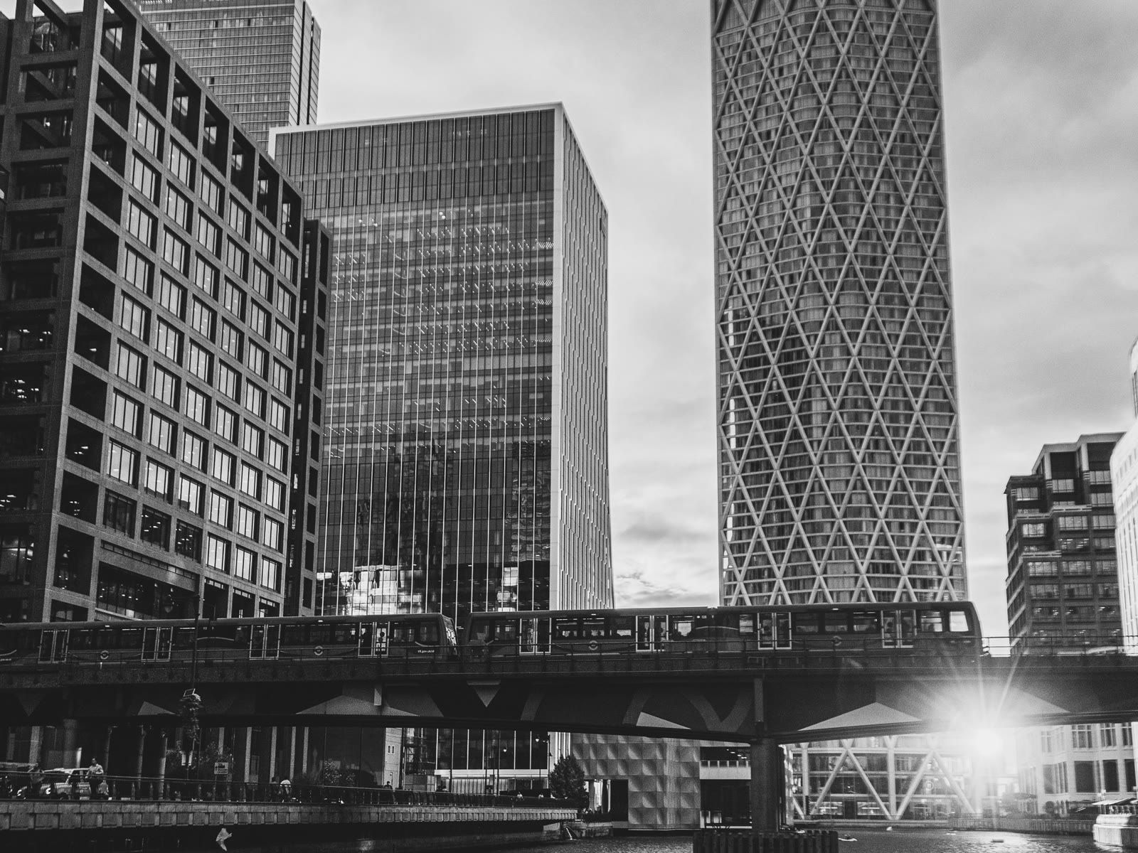 Canary Wharf towers above the DLR viaduct and the dock, in black and white