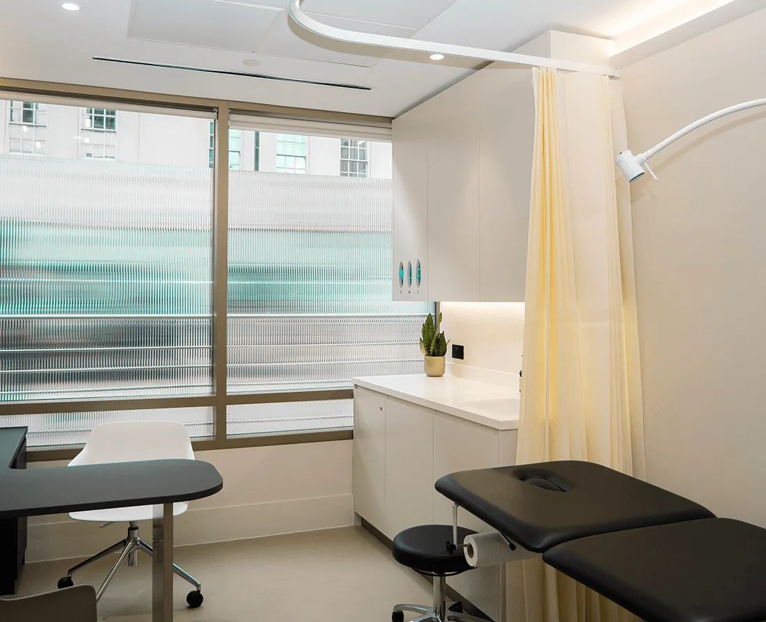 A consulting room at UNTIL Marylebone with a desk, chairs and an examination couch