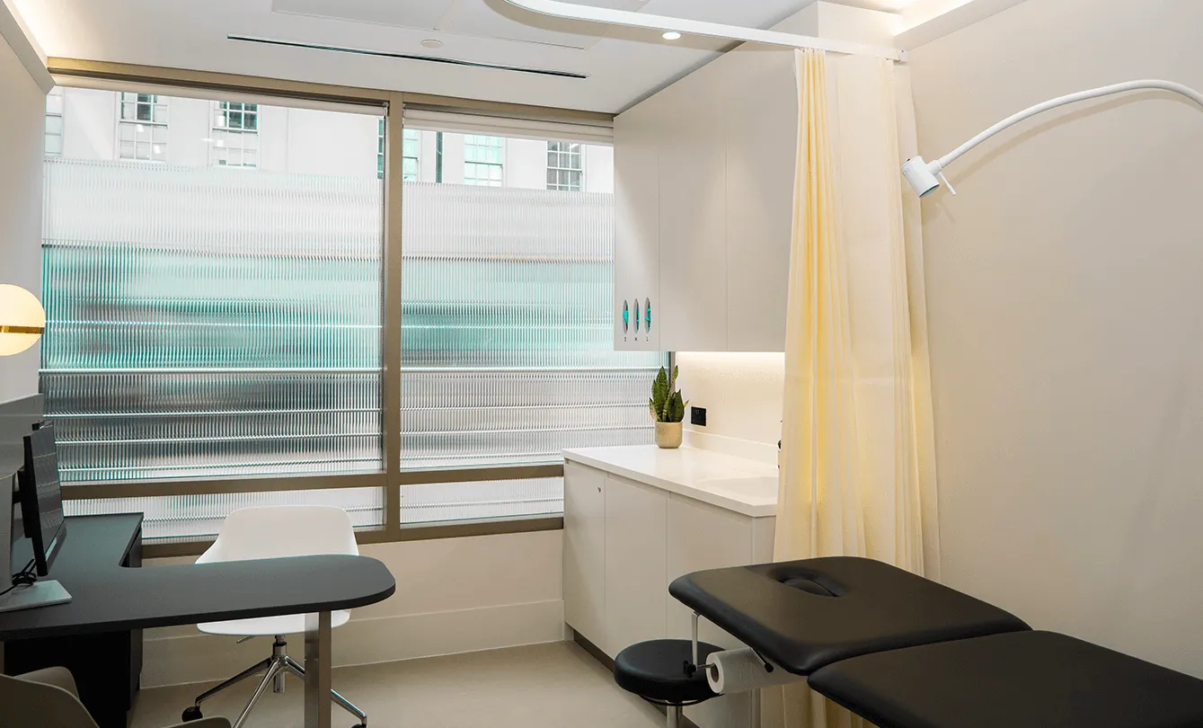 A consulting room at UNTIL Marylebone set up for a seated conversation, with a desk, chairs and an examination couch