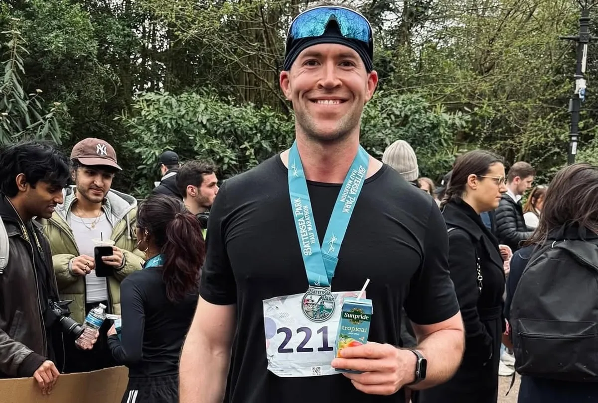 Jasper MacDermot after the Battersea Park half marathon, finisher medal on and a recovery drink in hand