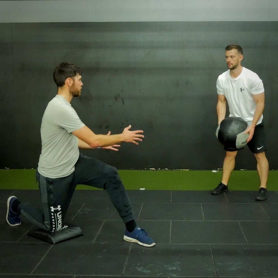 Kaizen coach guiding a kneeling medicine-ball drill in the gym