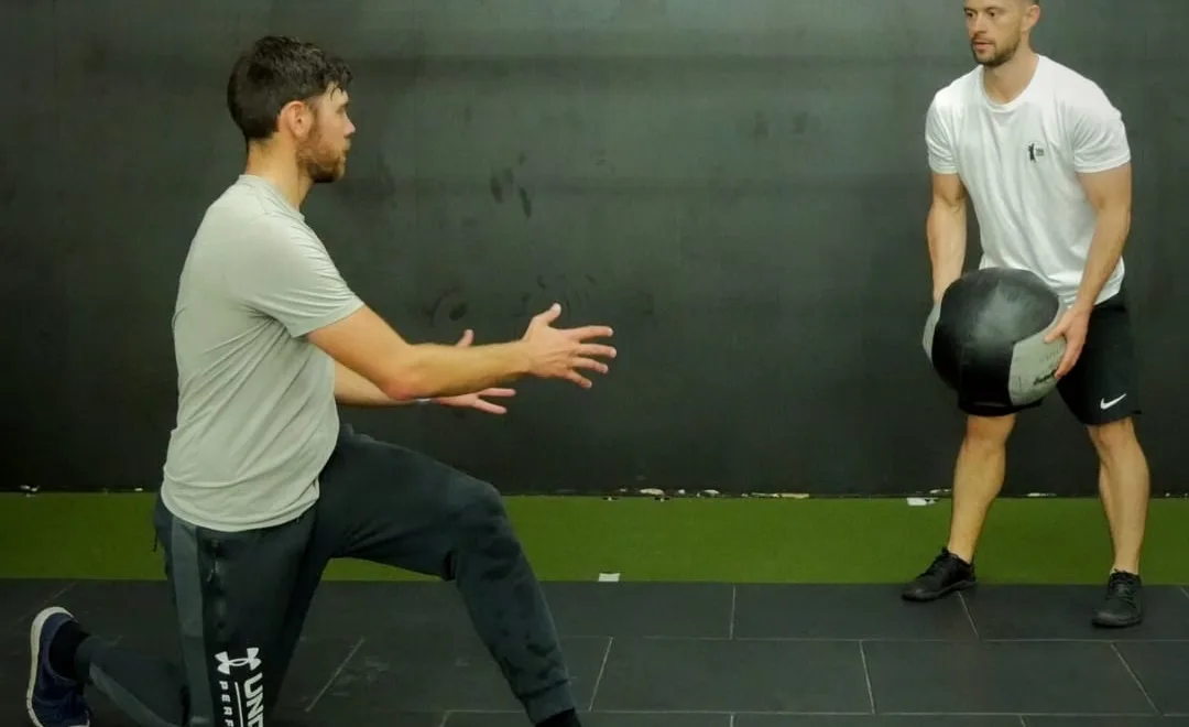 Kaizen coach guiding a kneeling medicine-ball drill in the gym