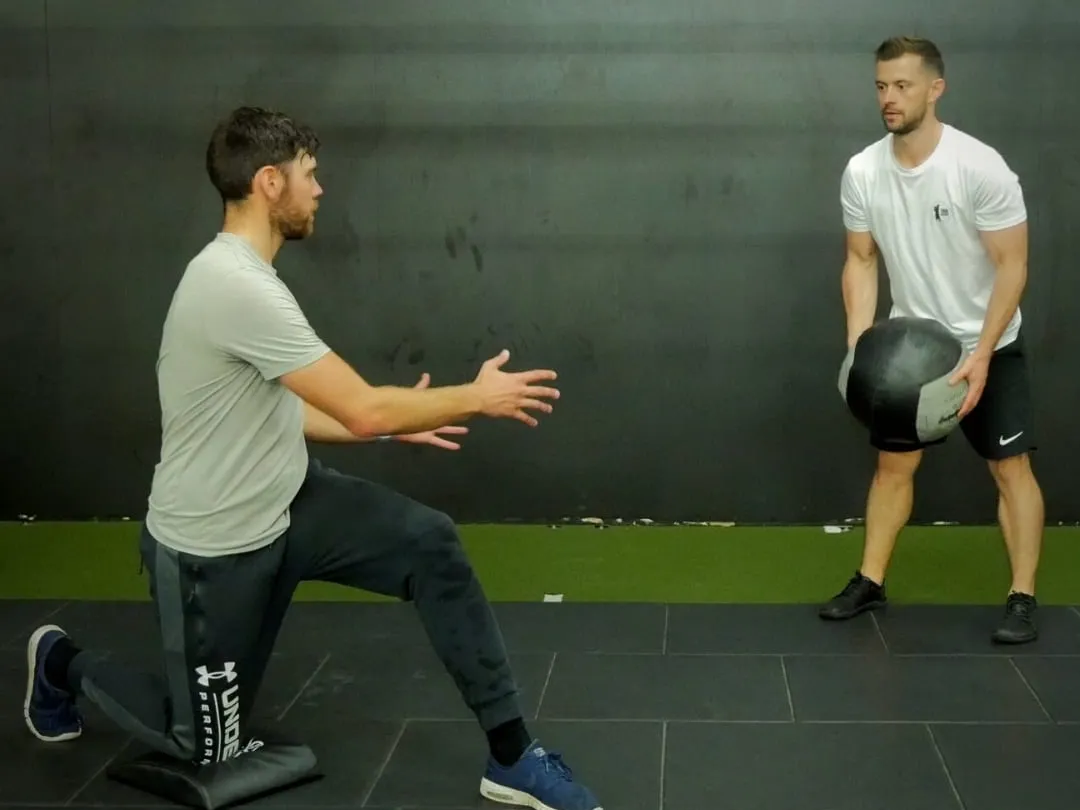 Kaizen coach guiding a kneeling medicine-ball drill in the gym
