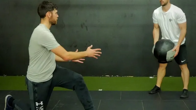 Kaizen coach guiding a kneeling medicine-ball drill in the gym