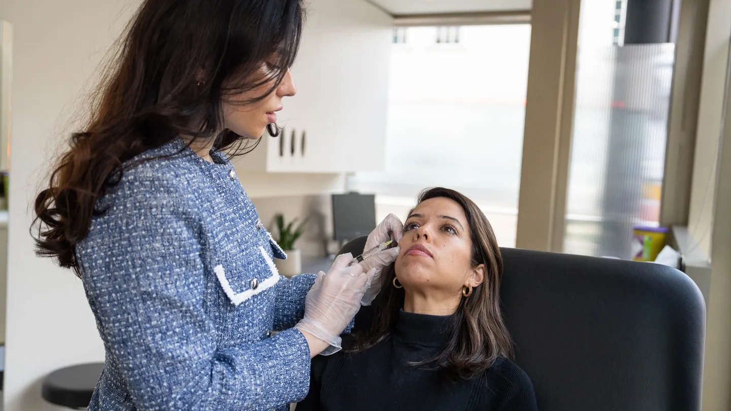 A practitioner gives a fine-needle injection to a client’s cheek in a treatment room