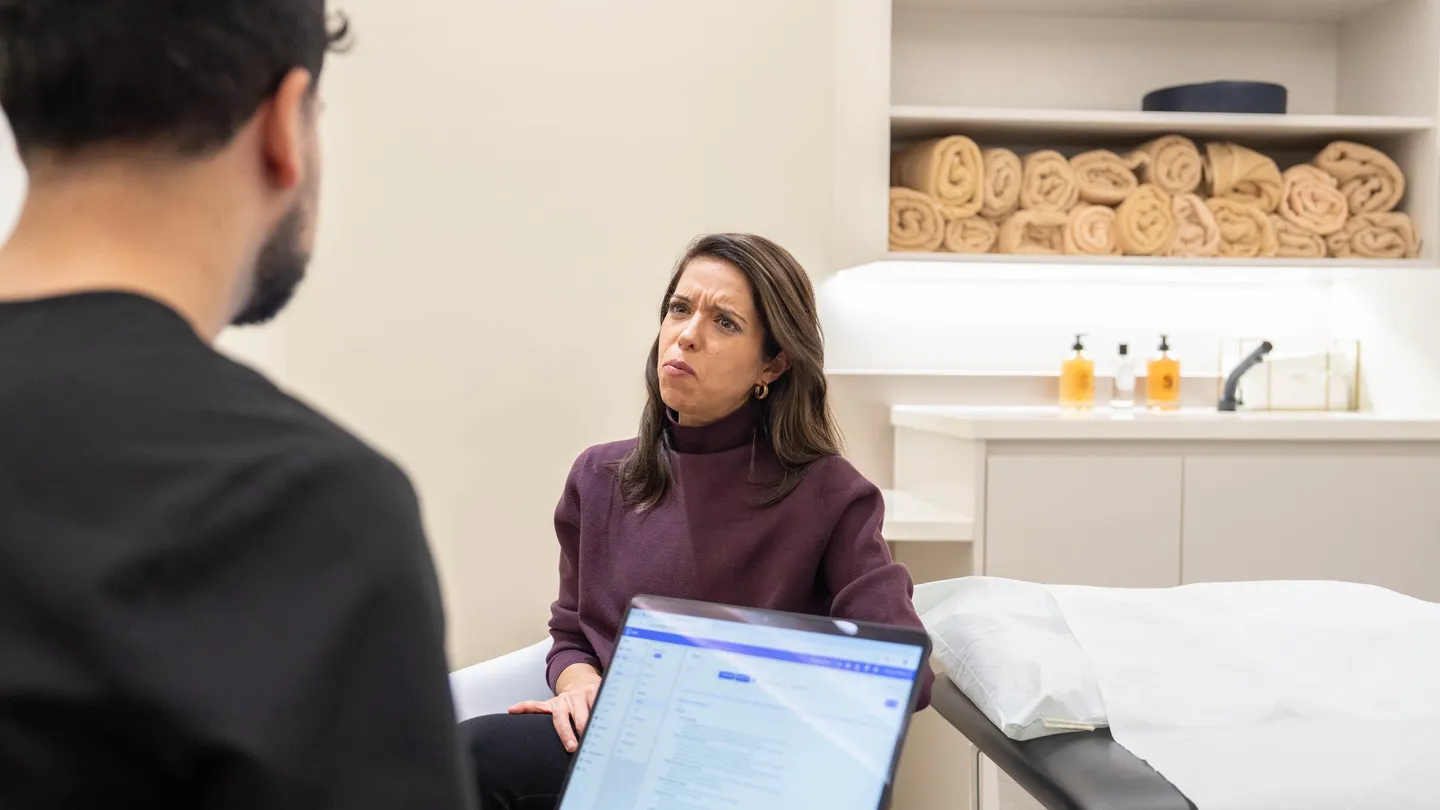 A client in a clinic room talks with a clinician who has notes open on a laptop
