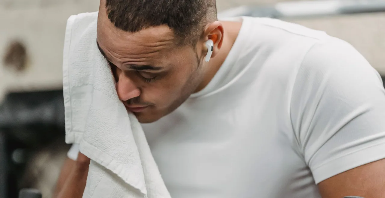Man pausing mid-workout to wipe his face with a towel — not seeing results at the gym after 40