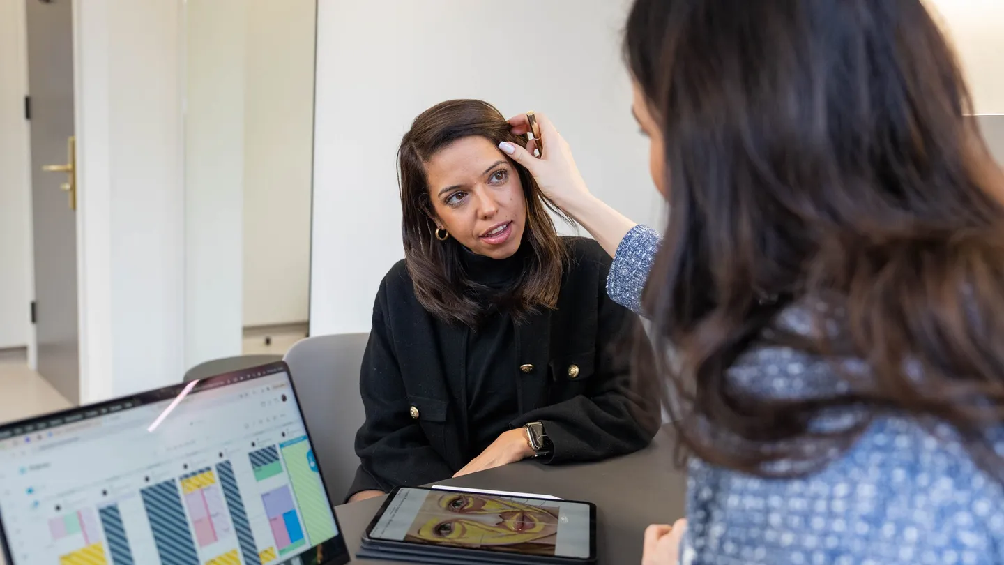 A practitioner lifts a client’s hair to look closely at her brow and the skin around her eyes during a consultation