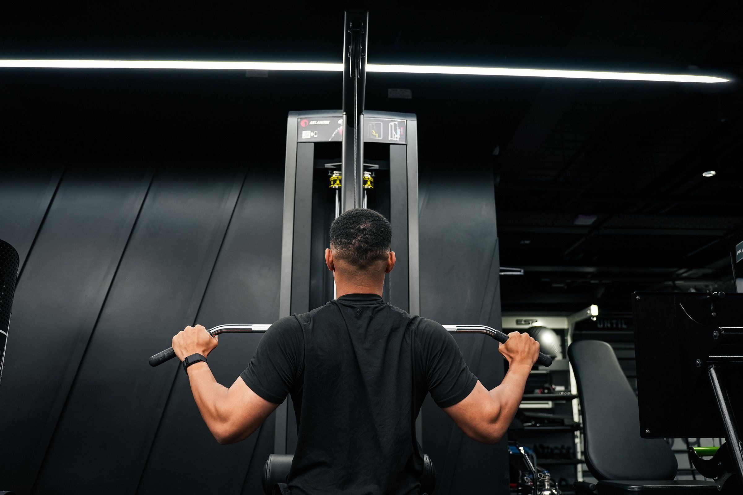 Steven Bartlett shot from behind at a lat pulldown machine with his hands wide on the bar
