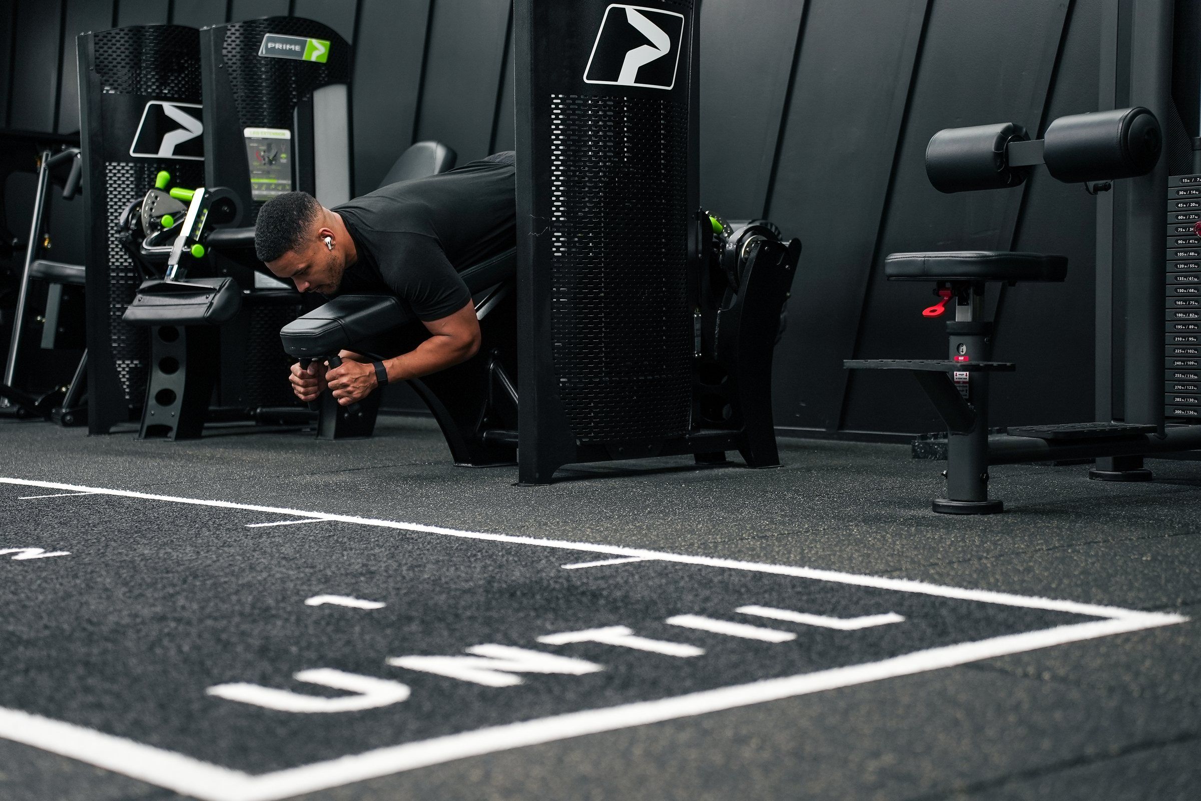 Steven Bartlett bent over a resistance machine with the UNTIL lettering marked out on the floor in front of him