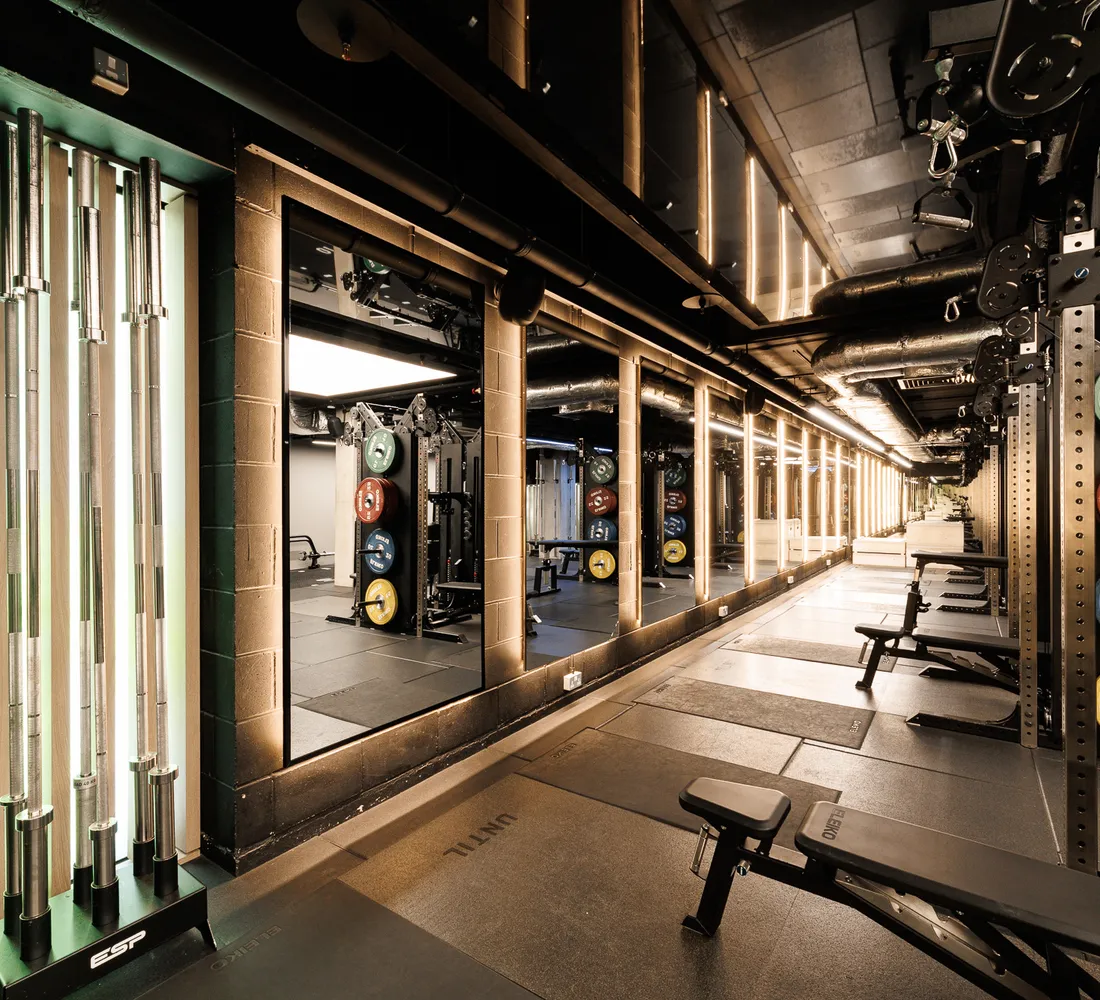 The mirrored barbell floor at UNTIL Soho, with racks, benches and loaded plates