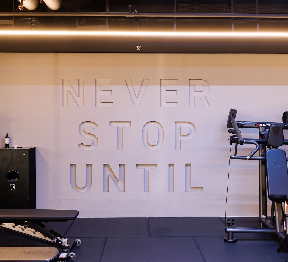 The "Never Stop Until" lettering on the wall at UNTIL Soho, beside a dumbbell rack, a bench and a resistance machine