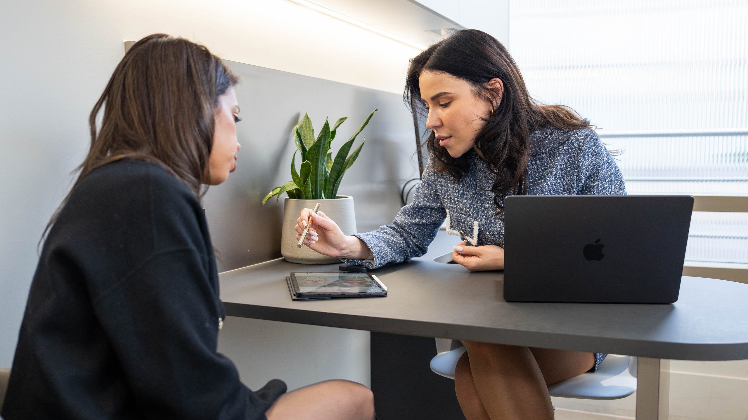 A practitioner and a client go through treatment options at a desk with a laptop and a tablet
