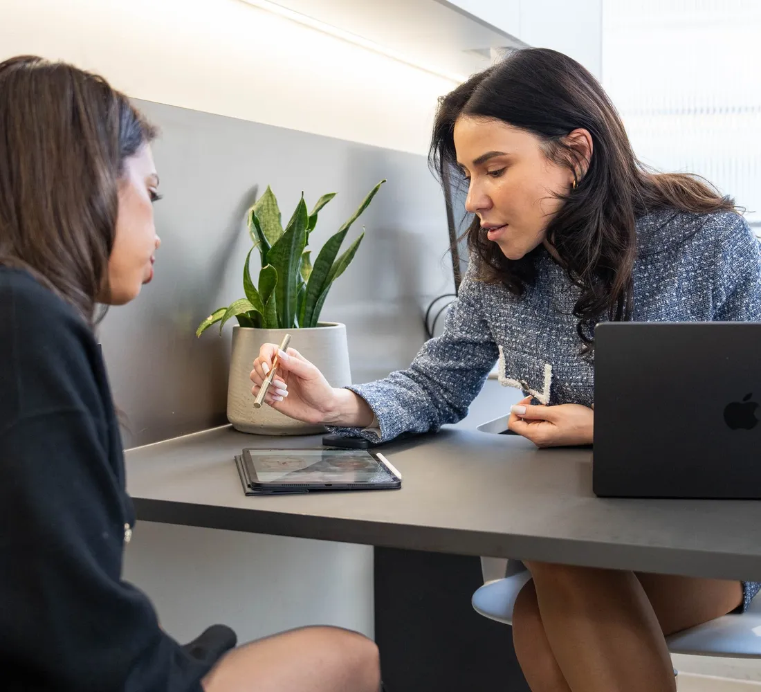 A practitioner and a client go through treatment options at a desk with a laptop and a tablet