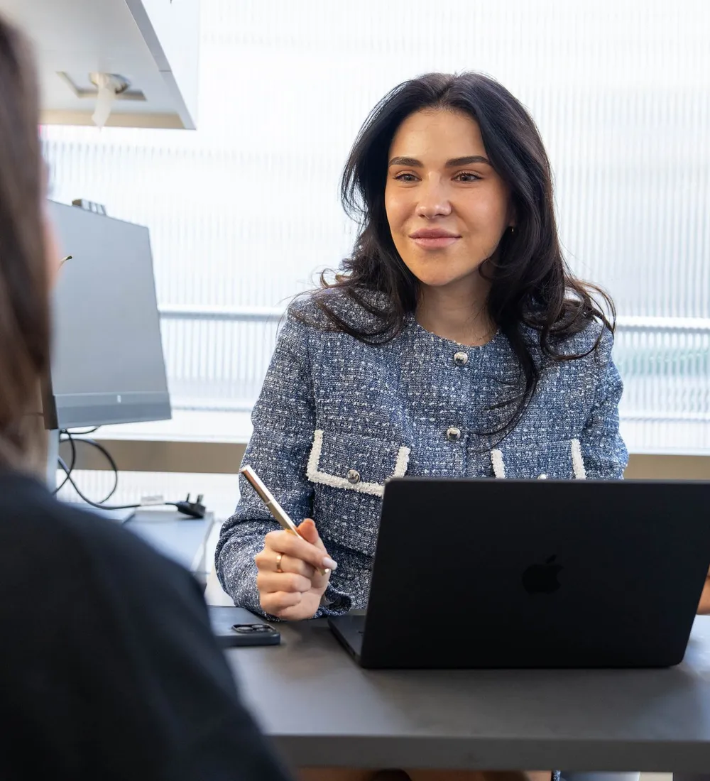 A practitioner talks a client through her options across a desk with a laptop open