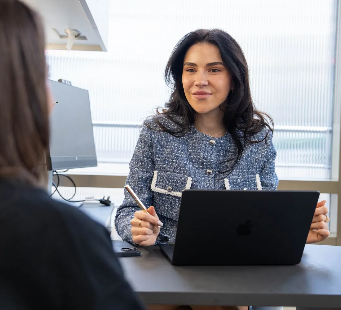 A practitioner talks a client through her options across a desk with a laptop open