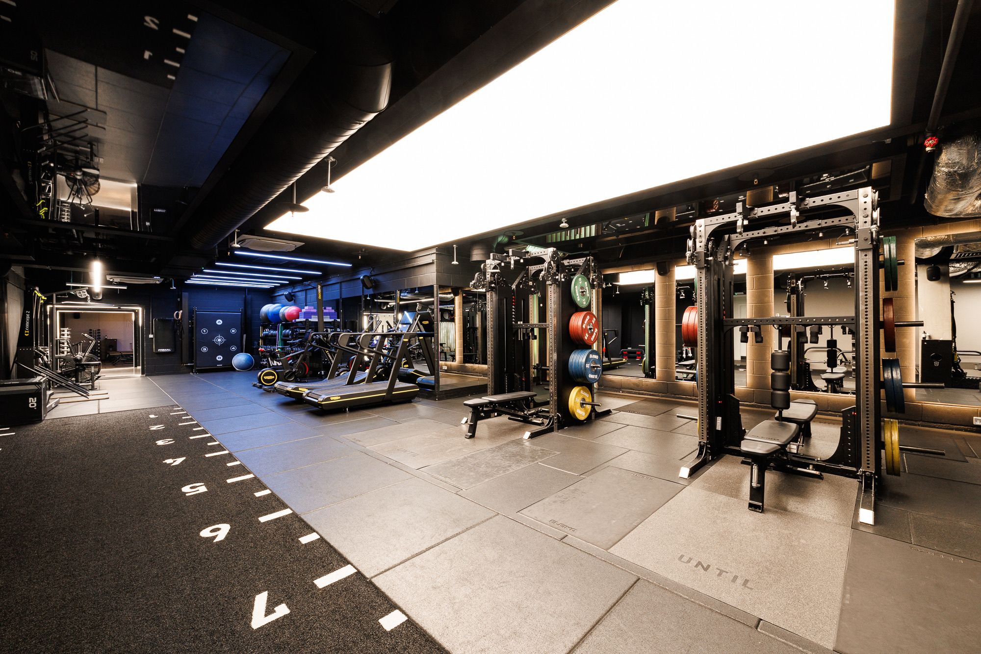 The strength and conditioning floor at UNTIL Soho, with squat racks, benches, and a sprint track