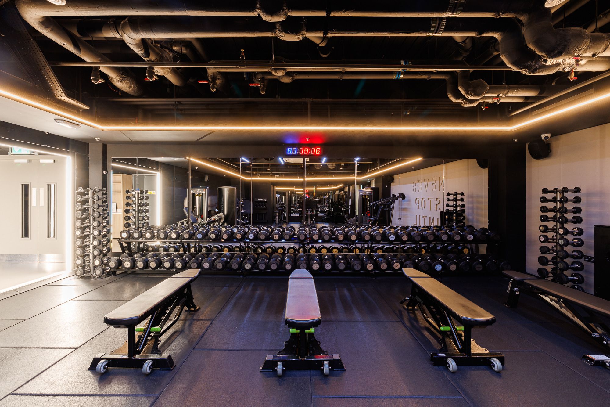 Dumbbell racks and adjustable benches by the mirrored free-weights wall at UNTIL Soho