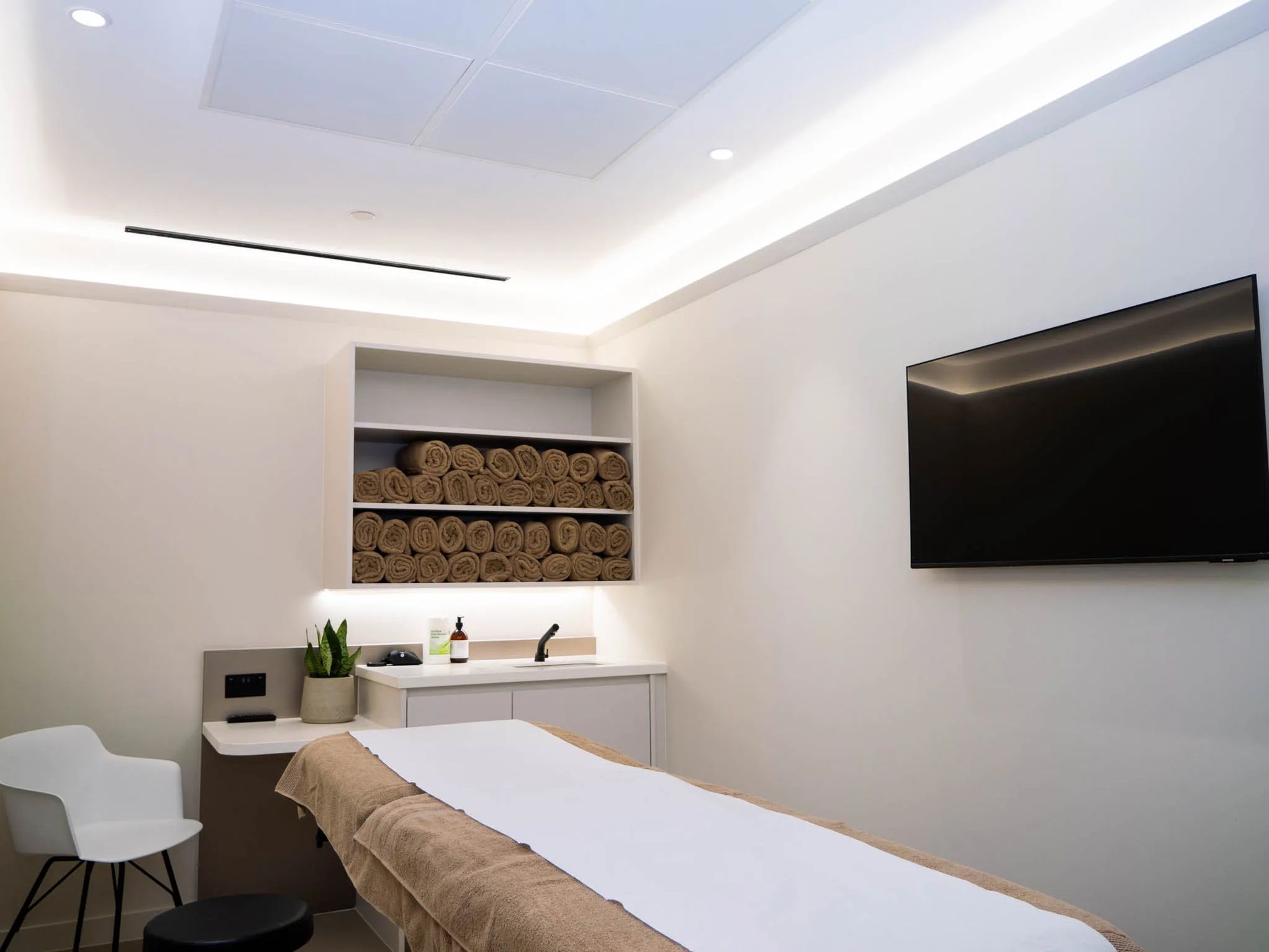 Treatment room at the UNTIL Marylebone clinic: a plinth, fresh towels and a wall-mounted screen.