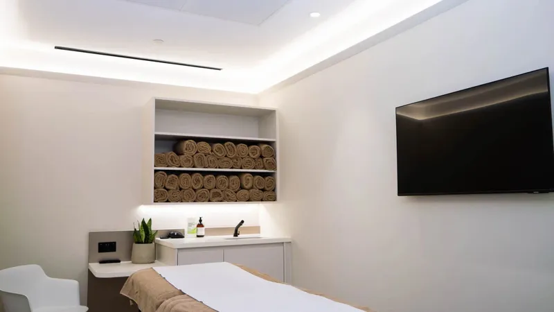 Treatment room at the UNTIL Marylebone clinic: a plinth, fresh towels and a wall-mounted screen.