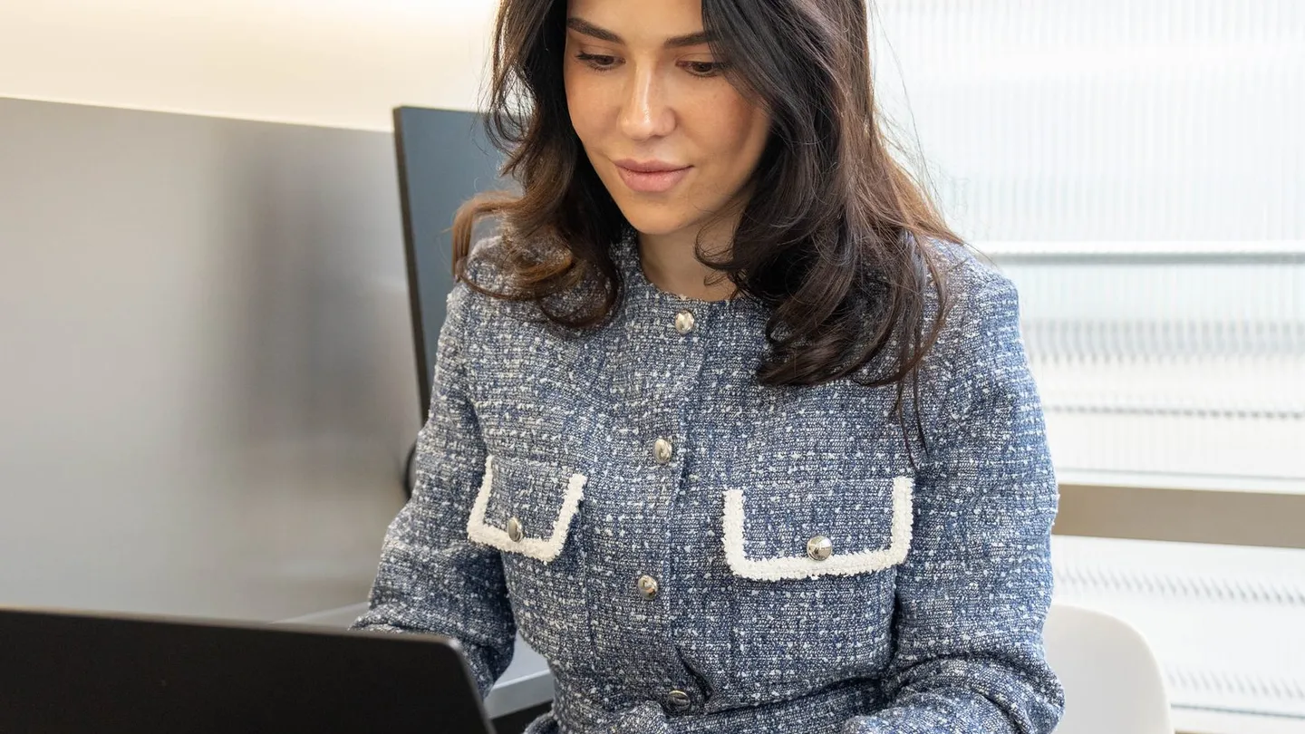 A practitioner in a blue tweed jacket reviews notes on a laptop at a desk